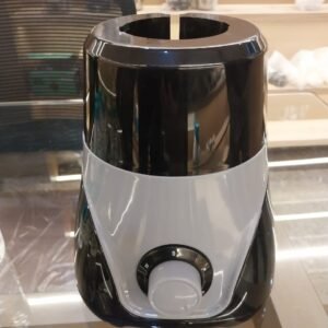 An image of a compact electric mixer grinder or blender base resting on a polished glass-top counter in an indoor showroom or workshop environment. The appliance features a dual-tone plastic body, with a glossy black upper and lower section split by a swooping, V-shaped light grey accent panel across the front face.