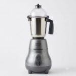 A high-resolution product shot of a metallic grey "oitons REAL GRIND" mixer grinder featuring a stainless steel jar with a transparent dome lid and a dark grey handle, set against a plain light background.