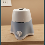 A crisp, close-up photograph of a compact electric mixer grinder base resting on a light-colored wooden countertop against a neutral beige wall. The appliance features a two-tone plastic body with a glossy white upper section and a matte, light-blue lower section that tapers down into a stable four-legged clover base with a white bottom trim.